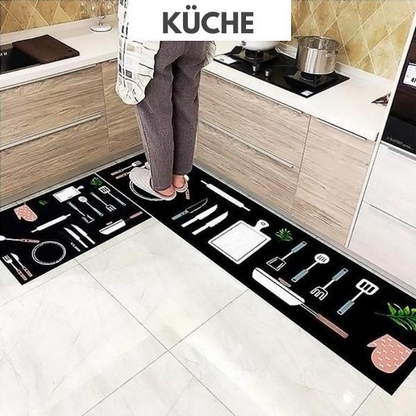 Woman standing on black coloured Anti Fatigue Kitchen rug printed with different types of kitchen utensils on it.